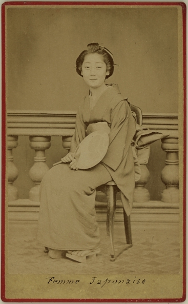 Photograph of a Japanese female in kimono, seated on a chair and holding a fan.  Ca. 1875-80