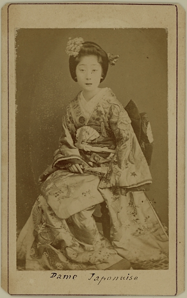 photograph of Japanese lady in kimono. She holds a folded fan.  Ca. 1875-80