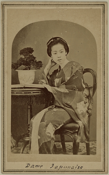 Japanese lady wearing kimono seated in chair besides a table.  Ca. 1875-80