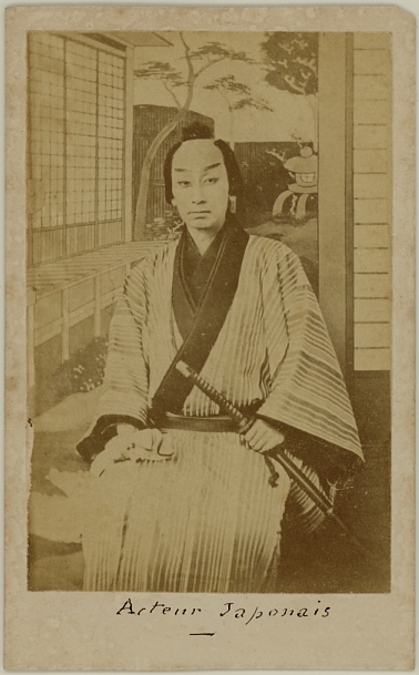 Japanese actor holding sword. Seated in front of the backdrop of a garden. Ca. 1875-80